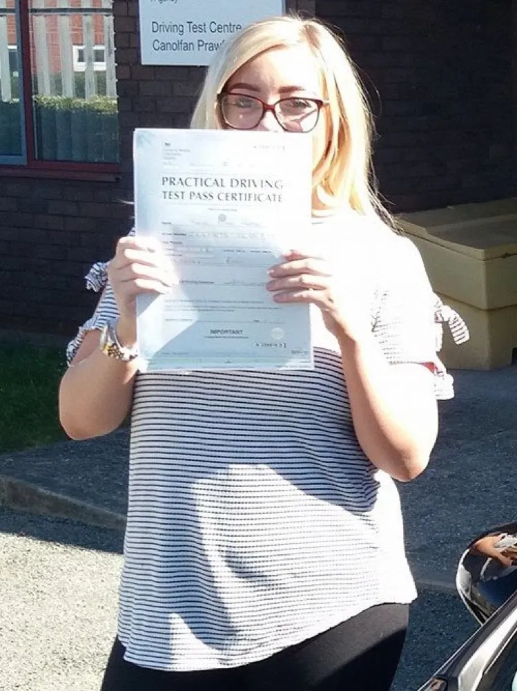 An SMS Driving School pupil holding their practical driving test pass certificate after passing at Rhyl test centre