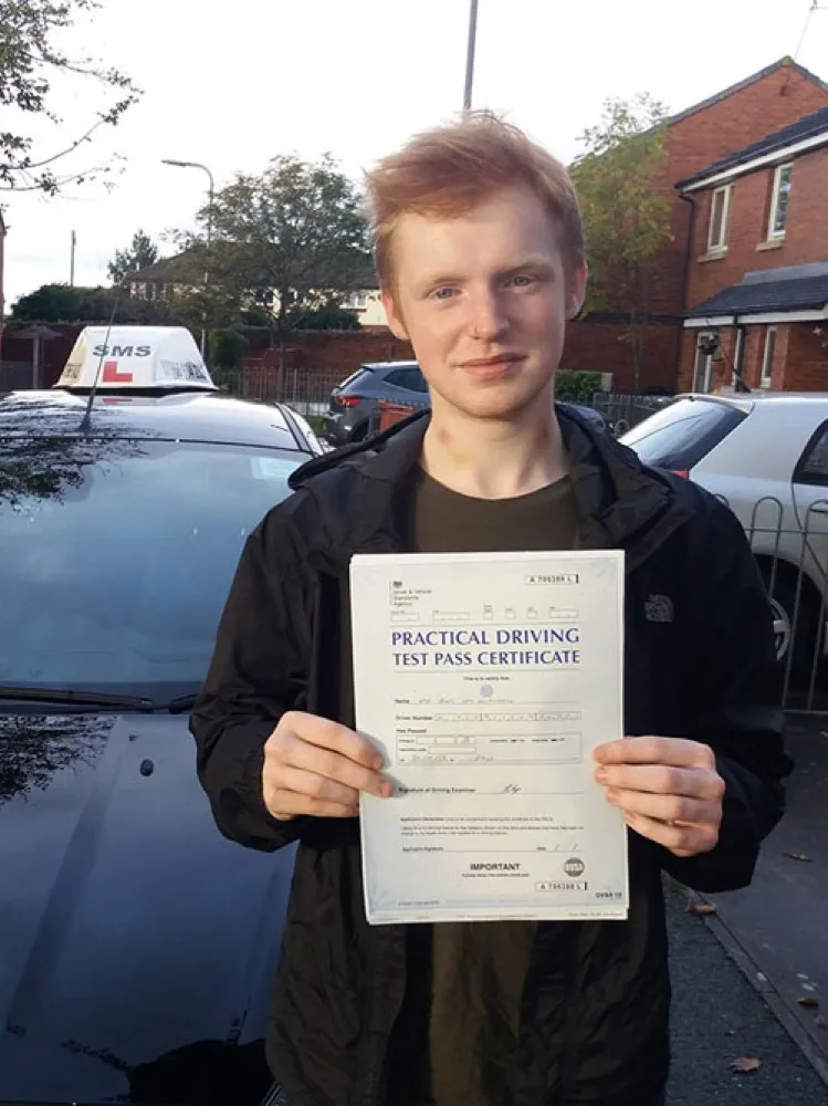 An SMS Driving School pupil holding their practical driving test pass certificate after passing at Rhyl test centre
