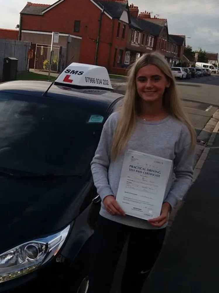 An SMS Driving School pupil holding their driving test pass certificate at Rhyl test centre