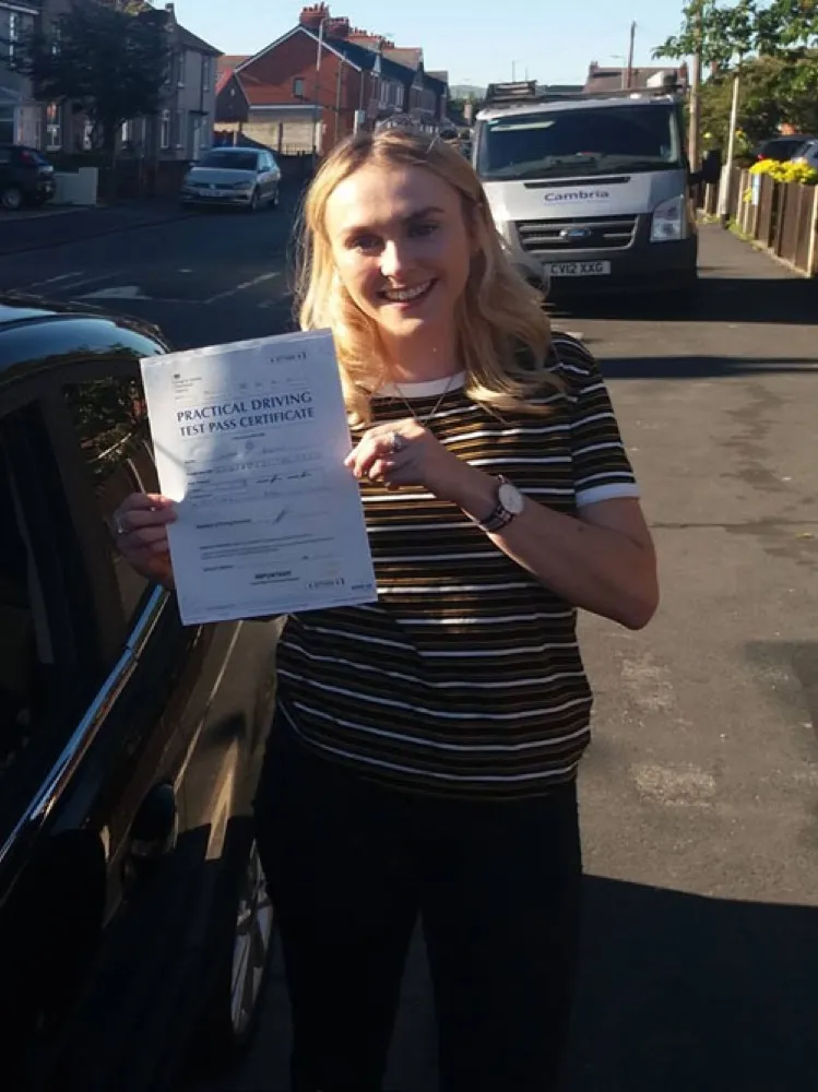 An SMS Driving School pupil holding their practical driving test pass certificate after passing at Rhyl test centre