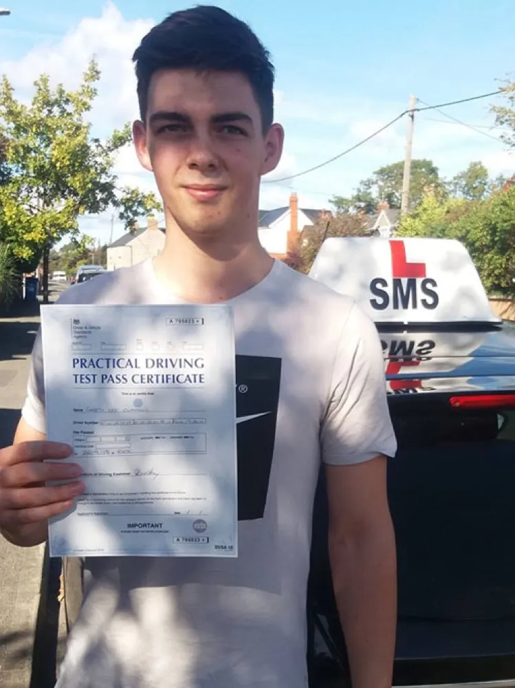 An SMS Driving School pupil holding their practical driving test pass certificate after passing at Rhyl test centre